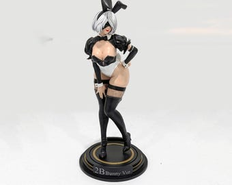 May include: A 2B Bunny Ver. figurine featuring a character with short white hair, a black blindfold, and black bunny ears. The figure wears a black and white leotard, black gloves, and black thigh-high stockings with fishnet details on a base.