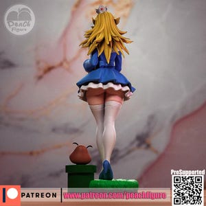 K&ouml;nnte beinhalten: Figur einer Figur mit langen, stacheligen blonden Haaren, die ein blaues Kleid mit einem wei&szlig;en R&uuml;schenrock und wei&szlig;en Oberschenkelstr&uuml;mpfen tr&auml;gt. Eine kleine Krone sitzt auf dem Kopf der Figur. Eine braune Goomba-Figur steht auf einer gr&uuml;nen Plattform.