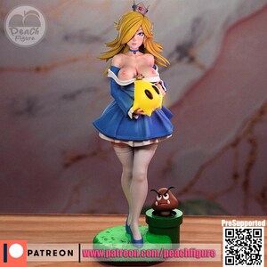 K&ouml;nnte beinhalten: Detaillierte Figur einer Figur mit blonden Haaren, die ein blaues Kleid und eine Krone tr&auml;gt. Die Figur h&auml;lt ein gelbes Objekt und steht auf einer gr&uuml;nen Basis mit einem Goomba und einem gr&uuml;nen Rohr. Die Figur ist mit "Peach Figure" beschriftet.