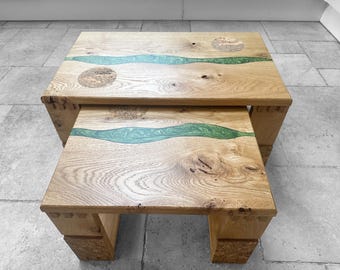 May include: Two wooden nesting tables with a green epoxy resin river design. The top table has a smooth surface and the bottom table has a more textured surface.