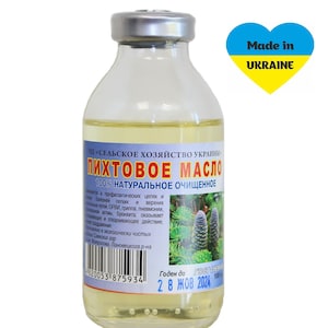 May include: A clear glass bottle with a silver cap containing a light yellow liquid. The label reads "ЧП «СЕЛЬСКОЕ ХОЗЯЙСТВО УКРАИНЫ» ПИХТОВОЕ МАСЛО 100% НАТУРАЛЬНОЕ ОЧИЩЕННОЕ" and includes a barcode. The bottle is sitting on a white background. The text "Made in UKRAINE" is written in yellow on a blue heart.