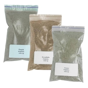 May include: Three clear plastic bags filled with dried herbs or spices. Each bag has a white label with Cyrillic text and the weight, 100 grams. The bags are sealed with a blue zipper closure. The contents vary in color, from light green to brown.