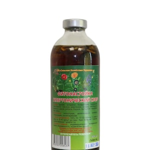 Può includere: Una bottiglia di vetro trasparente con tappo argentato, riempita con un liquido scuro ed erbe. La bottiglia ha un'etichetta verde con testo in lingua straniera e illustrazioni floreali. Il prodotto è di 250 ml.