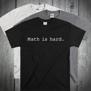 May include: Three t-shirts in black, white, and gray with the text "Math is hard." printed in white on the black t-shirt.