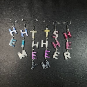 May include: A set of six colorful earrings, each featuring a different letter, spelling out the word "HEATHER". The earrings are made of resin and have a marbled effect.