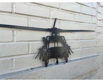 Könnte beinhalten: Schwarze Metall-Wandkunst, die einen Hubschrauber darstellt, montiert an einer weißen Backsteinmauer. Der Hubschrauber hat detaillierte Ausschnitte des Cockpits, der Rotoren und anderer Komponenten. Das Kunstwerk ist für die Wandmontage konzipiert.