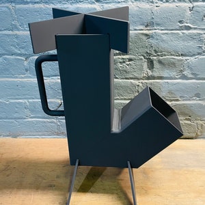 May include: A black metal wood-burning stove with a handle and four legs. The stove has a square firebox and a rectangular chimney.