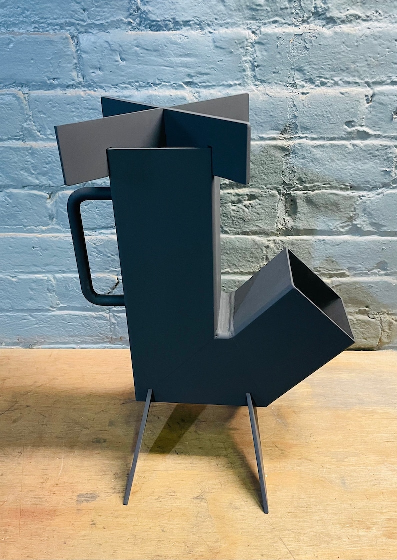May include: A black metal wood-burning stove with a handle and four legs. The stove has a square firebox and a rectangular chimney.