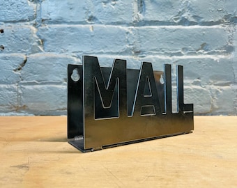 May include: A black metal mail holder with the word "MAIL" cut out in the front. The holder has two holes on the side for hanging.