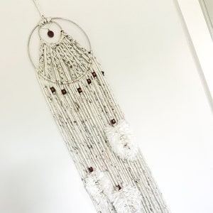 May include: White macrame wall hanging with wooden beads and white pom poms.