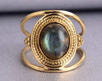 Può includere: Anello in oro con una grande pietra preziosa ovale iridescente incastonata in una lunetta decorativa. L'anello ha un design a doppia fascia.
