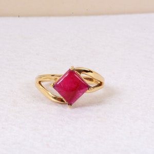 Puede incluir: Un anillo de oro con una piedra preciosa rosa brillante de forma cuadrada.
