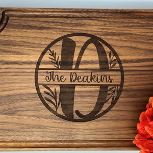 May include: A personalized walnut wood cutting board with a decorative circle design featuring the letter "D" and the text "The Deakins".