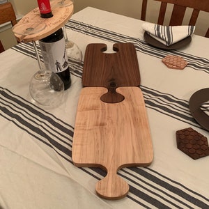 May include: Two wooden serving boards in a puzzle piece design, one light and one dark. A wine bottle and two wine glasses are held by a wooden wine glass holder. The holder has the text "Time For Wine".