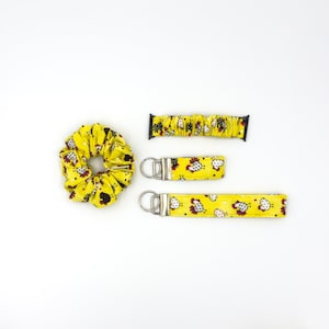 May include: A set of three yellow fabric accessories with a chicken print. The set includes a hair scrunchie, a watch band, and a keychain.