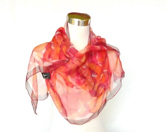 Op de afbeelding: Een vierkante, transparante sjaal in tinten rood, oranje en roze, gedrapeerd over een mannequin. De sjaal heeft een abstract ontwerp met een donkerrode rand. De stof lijkt licht en vloeiend, geschikt voor warmer weer.