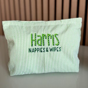 K&ouml;nnte beinhalten: Ein hellgr&uuml;ner und wei&szlig; gestreifter Stoffbeutel mit dem gestickten Text "Harris NAPPIES & WIPES" in Gr&uuml;n. Der Beutel ist rechteckig und scheint aus einem strukturierten Seersucker-Stoff zu bestehen.