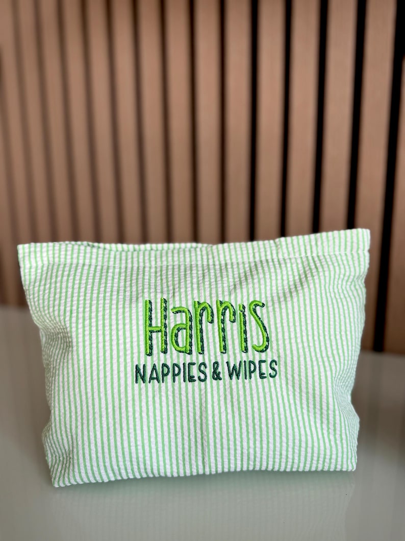 K&ouml;nnte beinhalten: Ein hellgr&uuml;ner und wei&szlig; gestreifter Stoffbeutel mit dem gestickten Text "Harris NAPPIES & WIPES" in Gr&uuml;n. Der Beutel ist rechteckig und scheint aus einem strukturierten Seersucker-Stoff zu bestehen.