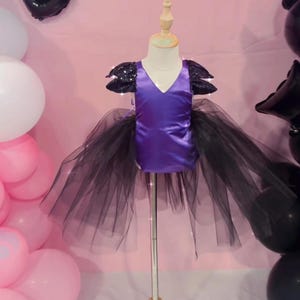 Könnte beinhalten: Lilafarbener Satin-Oberteil mit schwarzen Paillettenärmeln und einem schwarzen Tüllrock. Das Oberteil hat einen V-Ausschnitt und der Rock ist vielschichtig und weit.