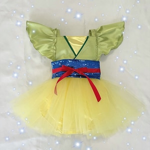 May include: A yellow tulle tutu with a green satin bodice and blue and red sequined belt. The bodice has a V-neck and short, ruffled sleeves.
