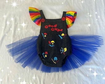 Puede incluir: Un mono de bebé de mezclilla con una falda de tul azul. El mono tiene mangas de arcoíris y dice "Good Guys" en letras rojas. El mono está decorado con varias imágenes de dibujos animados de colores.
