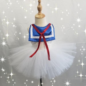 May include: White tulle tutu skirt with a blue and white sailor collar and red ribbon. The sailor collar has a white trim.
