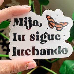 May include: A white sticker with black text that reads "Mijia, tu sigue luchando" and a small orange butterfly with black markings.