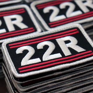 May include: A stack of black fabric patches with white embroidered text "22R" and two red stripes.