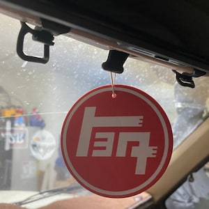 May include: Red round car air freshener with a white Toyota logo. The logo is a stylized "T" with three horizontal lines.
