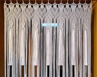 May include: White macrame wall hanging with a geometric pattern and tassels. The hanging is made of cotton cord and is approximately 3 feet wide.