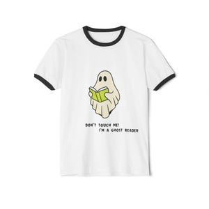 Op de afbeelding: Wit T-shirt met zwarte rand. Het heeft een cartoon spook dat een groen boek leest, met de tekst "DON'T TOUCH ME! I'M A GHOST READER" eronder. Een speels ontwerp, ideaal voor boekenliefhebbers en Halloween-fans.