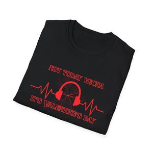 May include: Black t-shirt with red text and graphics. The text reads "NOT TODAY VECNA IT'S VALENTINE'S DAY" above a red graphic of headphones with a lightning bolt design and a heartbeat line. The shirt is folded.