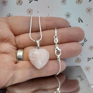 May include: A silver chain necklace with a heart-shaped pink rose quartz pendant. The necklace is on a hand and the chain is also shown separately.