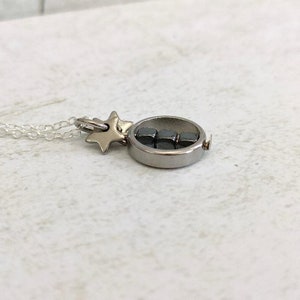Puede incluir: Un collar de plata con un dije de estrella y un dije redondo que contiene peque&ntilde;os cubos negros.