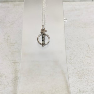 Puede incluir: Un collar de cadena de plata con un peque&ntilde;o colgante que presenta un c&iacute;rculo con una estrella en la parte superior y cuatro cuentas de plata en su interior.