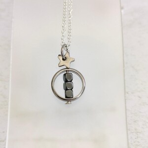 Puede incluir: Un collar de cadena de plata con un dije de estrella de plata y un anillo de plata con cuatro cuentas c&uacute;bicas negras colgando.