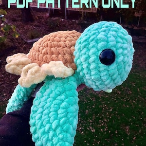 Puede incluir: Un juguete amigurumi de crochet en forma de tortuga turquesa y marrón con ojos negros. El juguete está siendo sostenido por una mano. El texto de la imagen dice "PDF PATTERN ONLY".