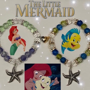 May include: Two beaded bracelets with charms. One bracelet has blue, green, and clear beads with a gold charm and a silver starfish charm. The other bracelet has purple, blue, green, and clear beads with a silver starfish charm. The bracelets feature images of Ariel and Flounder from The Little Mermaid.