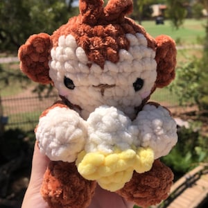 May include: A handmade crochet monkey plushie in brown, white, and yellow. The monkey has large ears, a smiling face, and is holding a yellow and white object. The plushie is soft and cuddly, perfect for a child's toy or nursery decor.