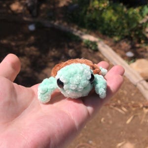 Puede incluir: Una peque&ntilde;a tortuga de ganchillo hecha a mano con caparaz&oacute;n marr&oacute;n y cuerpo y aletas verde menta. La tortuga tiene ojos negros. Un art&iacute;culo lindo y caprichoso.
