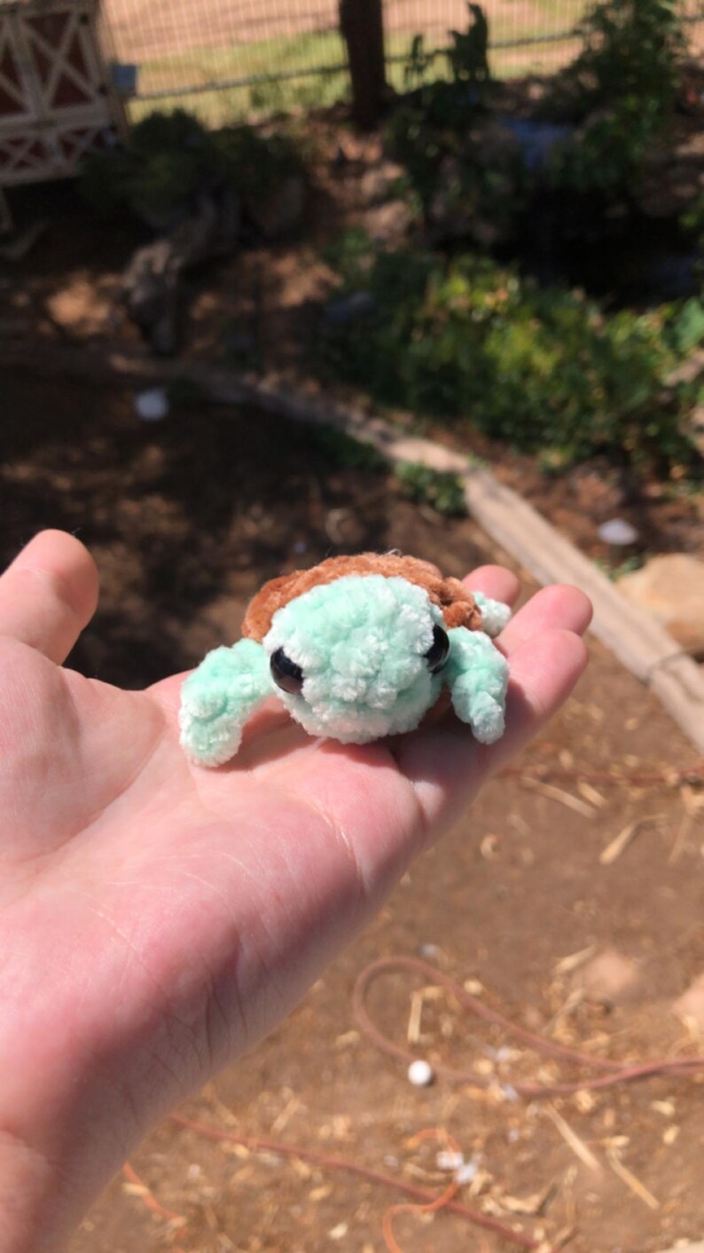 Puede incluir: Una peque&ntilde;a tortuga de ganchillo hecha a mano con caparaz&oacute;n marr&oacute;n y cuerpo y aletas verde menta. La tortuga tiene ojos negros. Un art&iacute;culo lindo y caprichoso.