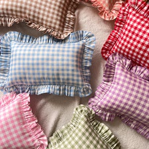 May include: A collection of rectangular scatter cushions featuring a gingham check pattern in various colours including brown, peach, red, light blue, purple, pink, and sage green. Each cushion is finished with a decorative ruffled fabric border.