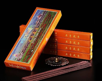 Op de afbeelding: Een stapel oranje dozen met Chinese karakters en een afbeelding van een tempel op de voorkant. De dozen bevatten wierookstokjes, die op de voorgrond te zien zijn. De wierookstokjes zijn bruin en hebben een ruwe textuur.