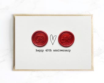 Op de afbeelding: Een witte kaart met een bruine rand toont twee rode zegels, een hart en de tekst "happy 40th anniversary". De zegels hebben de letters "R" en "M" in elegant schrift. Een eenvoudig, elegant ontwerp.