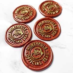 May include: Five red wax seals with a gold design of Santa Claus's face and the words "North Pole Official Seal".
