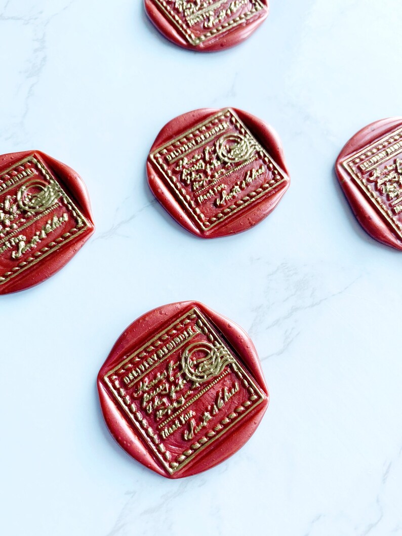 Puede incluir: Sellos de cera rojos con texto dorado en relieve y bordes decorativos esparcidos sobre una superficie de m&aacute;rmol blanco. Los sellos tienen un centro cuadrado con esquinas redondeadas y un borde exterior circular. El texto dice "Hours of Joy, Thank You, Sweetest of Dad."