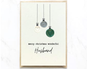 Op de afbeelding: Een kerstkaart met een crèmekleurige achtergrond en een bruine rand. De kaart toont drie decoratieve waszegels in wit, grijs en groen, hangend aan stippellijnen. De tekst luidt "merry christmas wonderful Husband."
