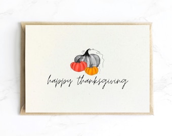 Op de afbeelding: Thanksgiving-wenskaart met een aquarelillustratie van drie pompoenen in oranje, grijs en rood. De woorden "happy thanksgiving" zijn in een sierlijk schrift onder de pompoenen geschreven. De kaart heeft een crèmekleurige achtergrond en een bruine rand.