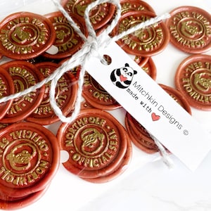May include: A package of 20 gold and red wax seals with the text "North Pole Official Seal" and a cartoon image of Santa Claus. The package is tied with twine and a white tag with a panda bear illustration and the text "Mitchkin Designs made with love".