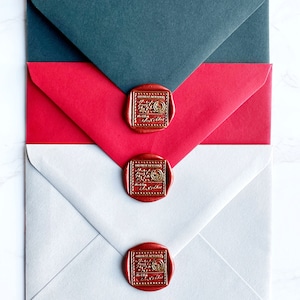 Puede incluir: Tres sobres en gris, rojo y blanco, sellados con sellos de cera rojos. Los sellos tienen un dise&ntilde;o dorado en relieve. Los sobres est&aacute;n dispuestos en un patr&oacute;n superpuesto, con el sobre gris en la parte superior.